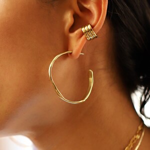 May include: Gold hoop earrings with a hammered texture. The earrings are large and have a thick, rounded shape.
