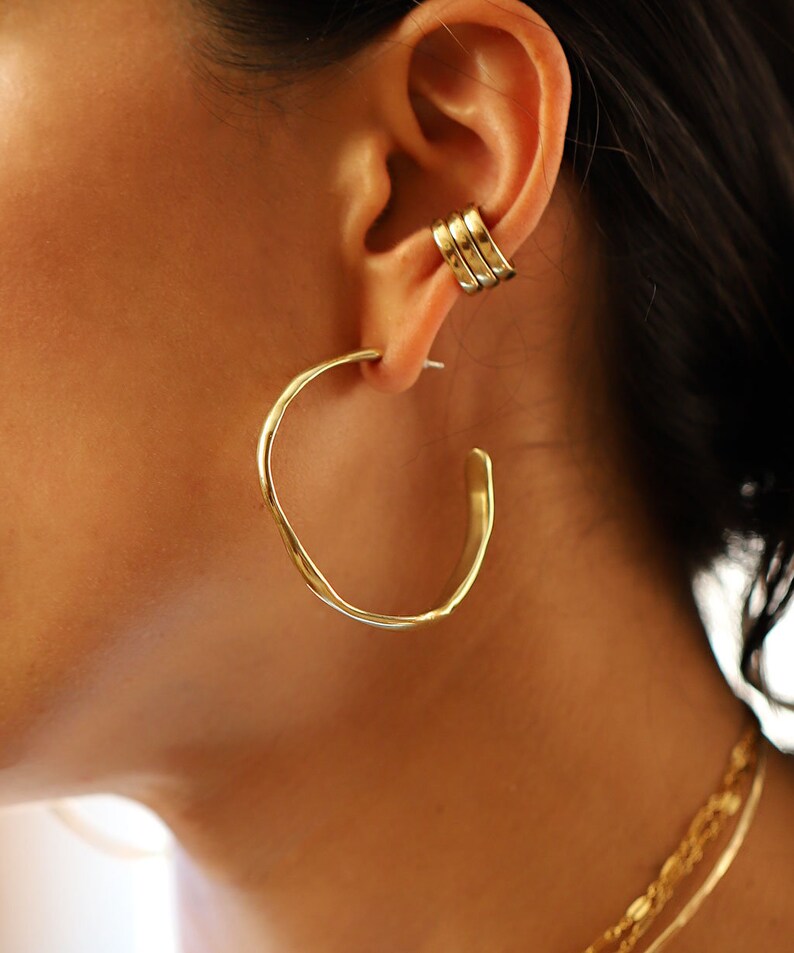 May include: Gold hoop earrings with a hammered texture. The earrings are large and have a thick, rounded shape.
