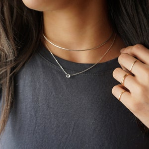 May include: A silver necklace with a small, clear gemstone pendant. The necklace is layered over a silver choker.