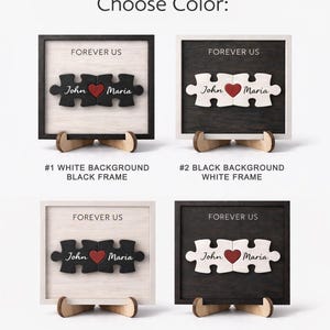 May include: Wooden puzzle art with the text "FOREVER US" and names "John" and "Maria". The puzzle pieces are connected with a red heart. The image shows four color options: white background with black frame, black background with white frame, white background with white frame, and black background with black frame.