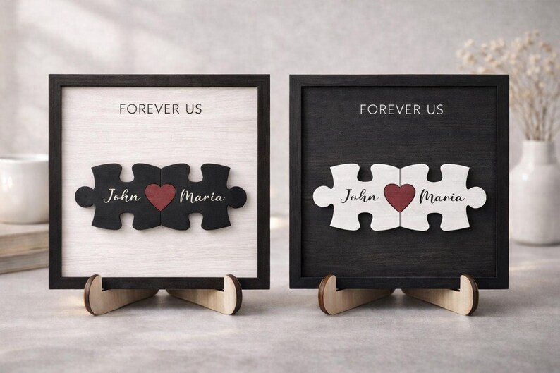 May include: Two framed wooden puzzle pieces, one black and one white, each with a heart and names "John" and "Maria." The text "FOREVER US" is above the puzzle pieces. The frames are displayed on wooden stands.
