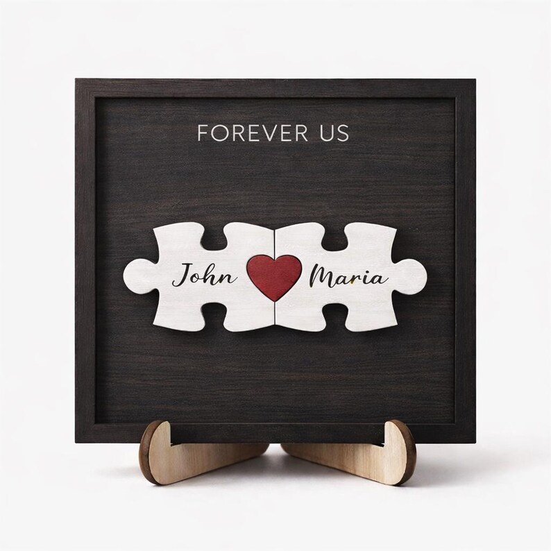 May include: A wooden framed sign with the words "FOREVER US" at the top. Two puzzle pieces with the names "John" and "Maria" and a red heart in the middle. The sign is displayed on a wooden stand.