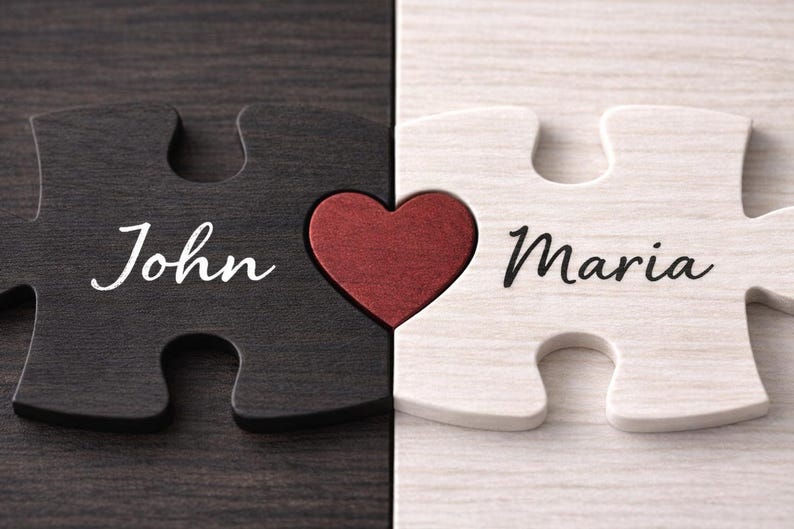 May include: Two wooden puzzle pieces, one black and one white, interlock with a red heart in the center. The black piece says "John" in white script, and the white piece says "Maria" in black script. A romantic gift.