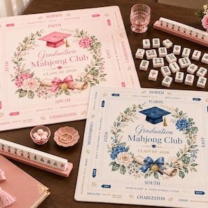 Könnte beinhalten: Zwei dekorative Mahjong Club Tischsets mit Blumen- und Abschlusskappen-Designs. Eines ist rosa mit einer rosa Kappe, das andere ist cremefarben mit einer blauen Kappe. Mahjong-Steine, ein rosa Buch und ein Glas sind ebenfalls sichtbar.