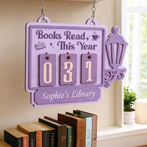 Puede incluir: Un letrero de madera lila con el texto "Books Read This Year" y el número "031". El letrero tiene un diseño de linterna decorativa y está personalizado con "Sophie's Library". Cuelga sobre una colección de libros.