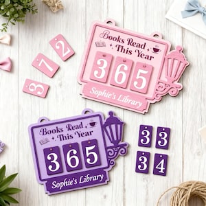 Puede incluir: Dos contadores de libros de madera, uno rosa y otro morado, con el texto "Libros leídos este año" y "365". El contador rosa tiene el nombre "Sophie's Library". Se incluyen fichas numéricas rosas y moradas adicionales.