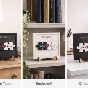 May include: A wooden puzzle piece sign with the words "FOREVER US". The puzzle pieces are black and white, with the names "John" and "Maria" and a red heart. The sign is displayed on a wooden stand.