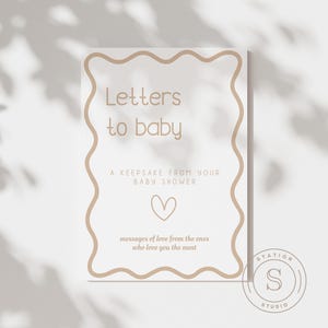 Może przedstawiać: Prostokątny znak z falistą obw&oacute;dką i napisem "Letters to baby". Znak zawiera tekst "A keepsake from your baby shower", grafikę serca oraz słowa "messages of love from the ones who love you the most."