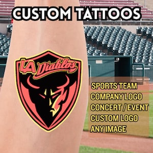 Puede incluir: Un tatuaje temporal con el texto "CUSTOM TATTOOS" en la parte superior. El diseño es un logotipo en forma de escudo con el texto "LA Diablos" y un gráfico de diablo. El texto adicional incluye "SPORTS TEAM", "COMPANY LOGO", "CONCERT / EVENT", "CUSTOM LOGO" y "ANY IMAGE".