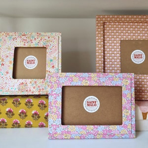 Pu&ograve; includere: Una collezione di cornici decorative con disegni floreali e motivi. Le cornici presentano una variet&agrave; di colori, tra cui rosa, giallo e marrone. Ogni cornice ha un'apertura centrale e un adesivo "SAINT MALO".