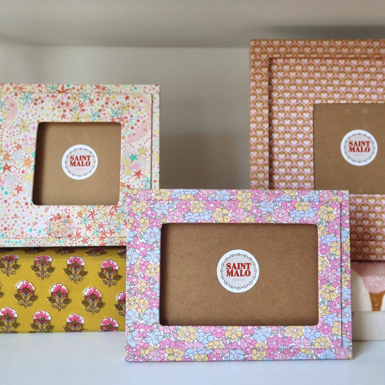 Pu&ograve; includere: Una collezione di cornici decorative con disegni floreali e motivi. Le cornici presentano una variet&agrave; di colori, tra cui rosa, giallo e marrone. Ogni cornice ha un'apertura centrale e un adesivo "SAINT MALO".