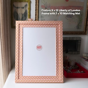 Pu&ograve; includere: Una cornice Liberty of London personalizzata di 23 x 30 cm con un passe-partout abbinato di 18 x 25 cm. La cornice presenta un motivo a cuori rosa e oro. Il logo Saint Malo &egrave; visibile.