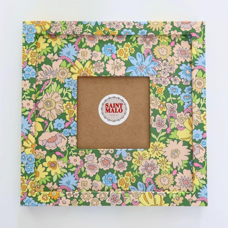 Pu&ograve; includere: Cornice quadrata con un motivo floreale nei toni del verde, giallo, rosa e blu. La cornice ha un'apertura centrale e un retro marrone. Un adesivo con la scritta "SAINT MALO DESIGNS" &egrave; sul retro.