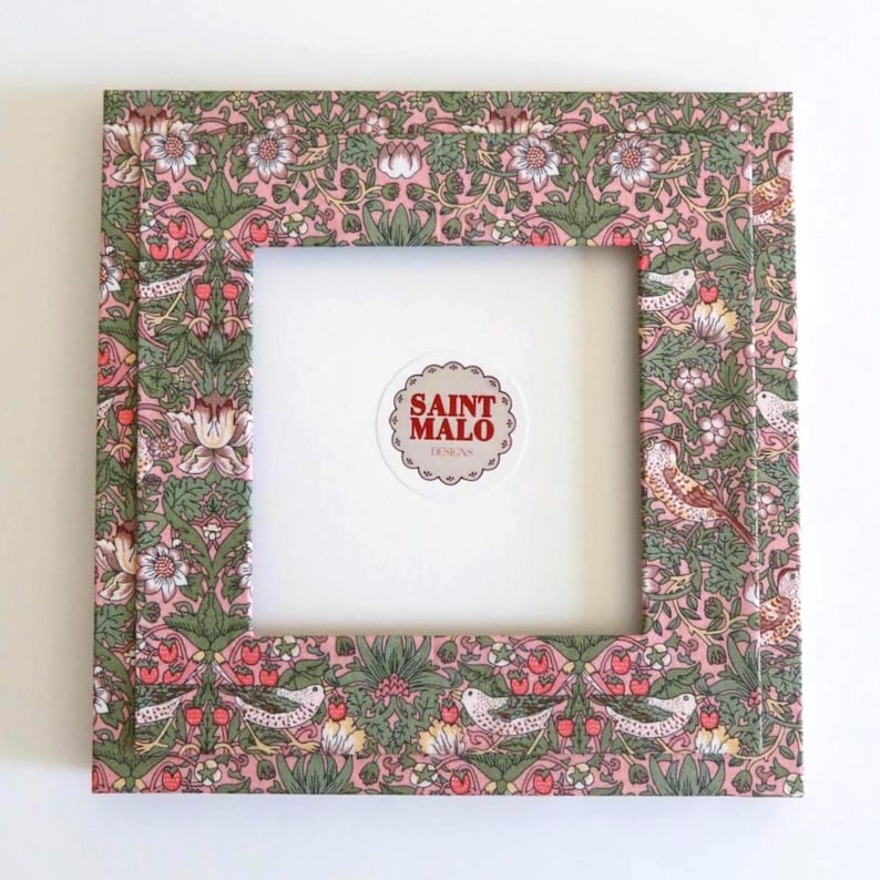 Pu&ograve; includere: Cornice quadrata con un motivo floreale e di uccelli in rosa, verde e bianco. La cornice ha un interno bianco e un adesivo con la scritta "SAINT MALO DESIGNS".