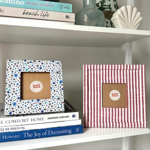 Pu&ograve; includere: Due cornici quadrate decorative. Una cornice ha un motivo a stelle blu e bianche, l'altra ha un motivo a righe rosse e bianche. Entrambe le cornici hanno un'apertura quadrata e un retro marrone con un adesivo "SAINT MALO".