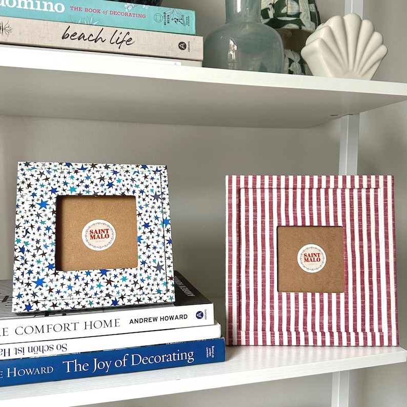 Pu&ograve; includere: Due cornici quadrate decorative. Una cornice ha un motivo a stelle blu e bianche, l'altra ha un motivo a righe rosse e bianche. Entrambe le cornici hanno un'apertura quadrata e un retro marrone con un adesivo "SAINT MALO".