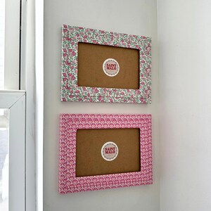 Pu&ograve; includere: Due cornici rettangolari con motivi floreali sono montate su un muro bianco. La cornice superiore ha un design floreale verde e rosa, mentre la cornice inferiore presenta un motivo floreale rosa. Ogni cornice ha un retro marrone e un adesivo "SAINT MALO".
