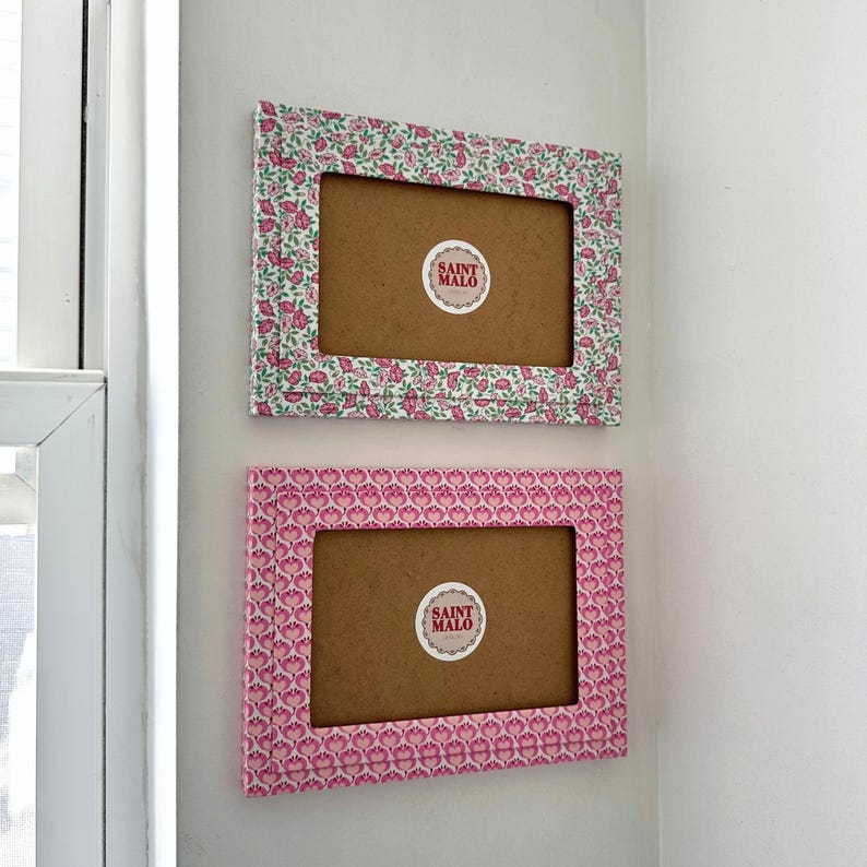 Pu&ograve; includere: Due cornici rettangolari con motivi floreali sono montate su un muro bianco. La cornice superiore ha un design floreale verde e rosa, mentre la cornice inferiore presenta un motivo floreale rosa. Ogni cornice ha un retro marrone e un adesivo "SAINT MALO".
