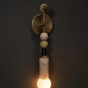 May include: A modern wall sconce with a brass finish and a series of decorative spheres in shades of green and pink. The sconce features a cylindrical base with a marble-like pattern and a glowing bulb at the bottom.