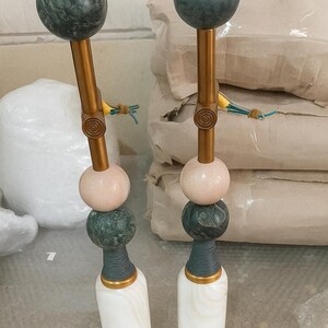 May include: Two decorative objects with a gold-colored stem, topped with a dark green sphere. The stem has a pink sphere, a dark green sphere, and a white base. The objects are likely decorative items or sculptures.