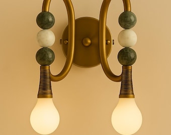 May include: A gold wall sconce with two light bulbs and green and white marble beads.