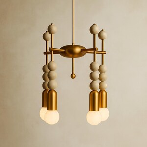 May include: A modern chandelier with a gold finish and a unique design. The fixture features multiple arms with cream-colored spheres and globe-shaped light bulbs. The overall aesthetic is a blend of mid-century modern and contemporary styles.