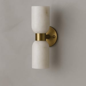 May include: A contemporary wall light with a white marble design and brass detailing. The light has a cylindrical form with rounded ends, joined by a brass band. It's mounted on a circular brass backplate. The dimensions are approximately 30 cm in height.