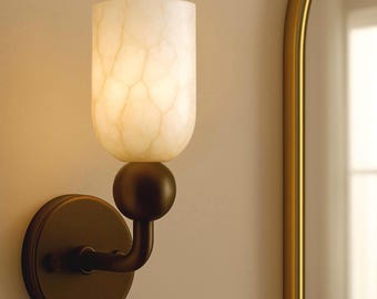 May include: A wall-mounted sconce with a cylindrical, off-white shade featuring a marbled pattern. The shade sits atop a dark brown sphere, connected to a circular base by a curved arm. The fixture is set against a neutral wall.