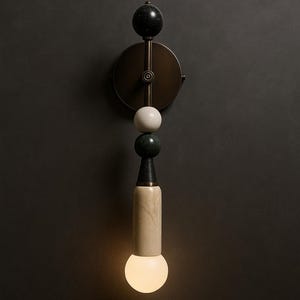 May include: A modern wall sconce with a brass finish and a decorative design. The sconce features a black marble sphere, a white sphere, a green marble sphere, and a cylindrical light fixture with a warm, glowing bulb.