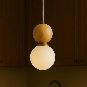 May include: A modern pendant light fixture with a spherical frosted glass shade and a wooden sphere above it. The light hangs from a brown cord, and is set against a dark wood background.