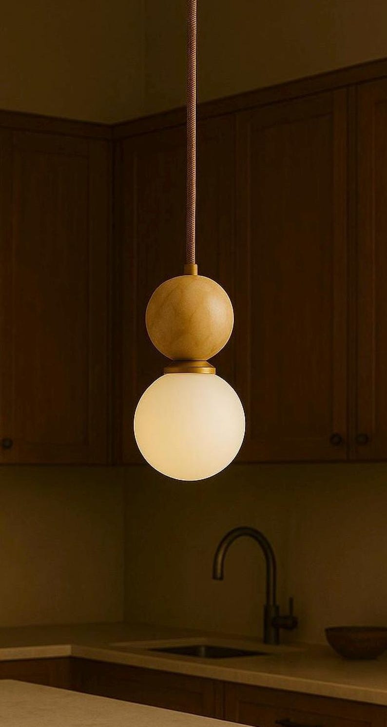 May include: A modern pendant light fixture with a spherical frosted glass shade and a wooden sphere above it. The light hangs from a brown cord, and is set against a dark wood background.
