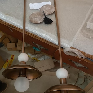 May include: Two pendant lights with copper-colored shades and stems. Each light has a white globe at the top and a frosted glass bulb at the bottom. The lights are suspended from the ceiling.