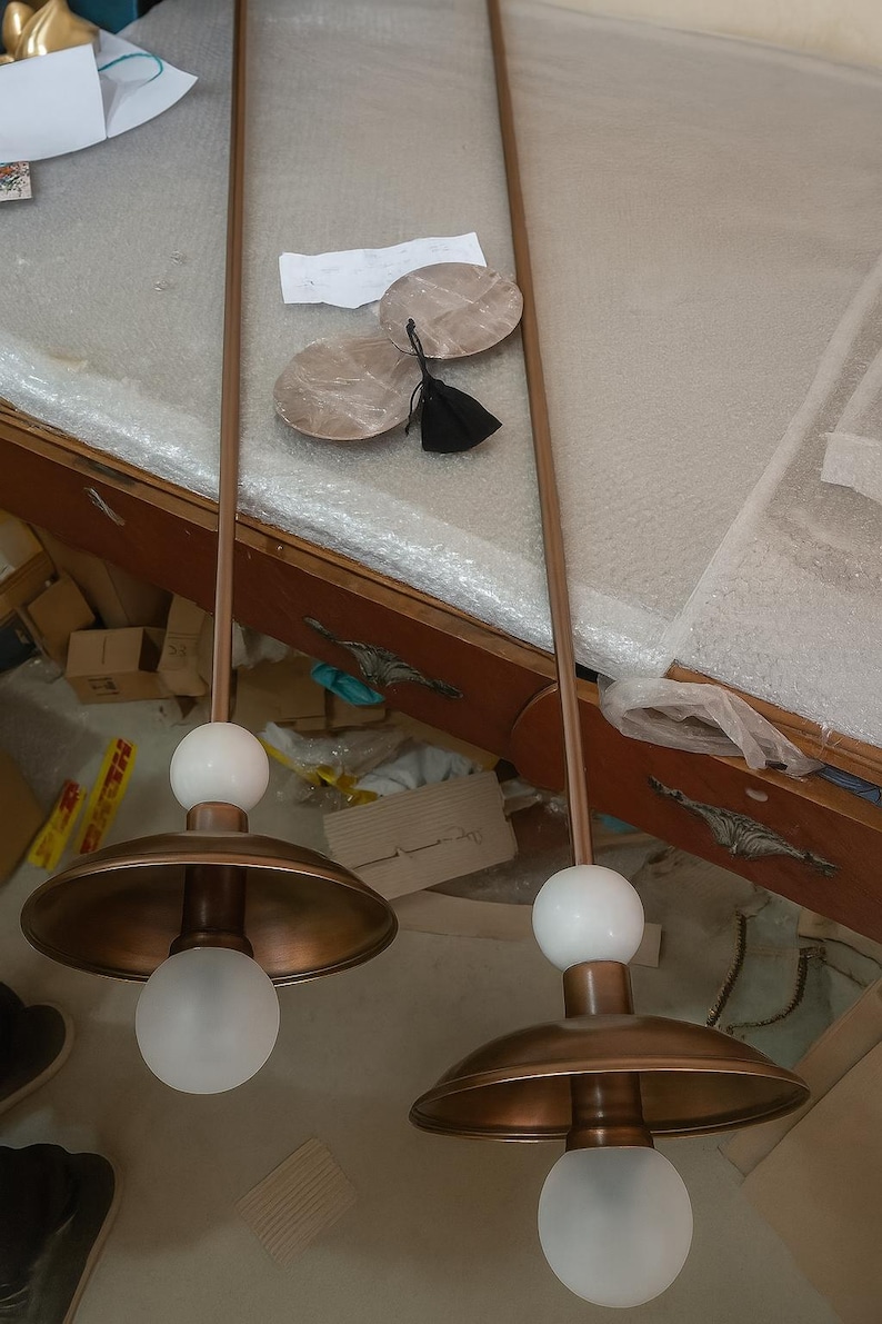 May include: Two pendant lights with copper-colored shades and stems. Each light has a white globe at the top and a frosted glass bulb at the bottom. The lights are suspended from the ceiling.