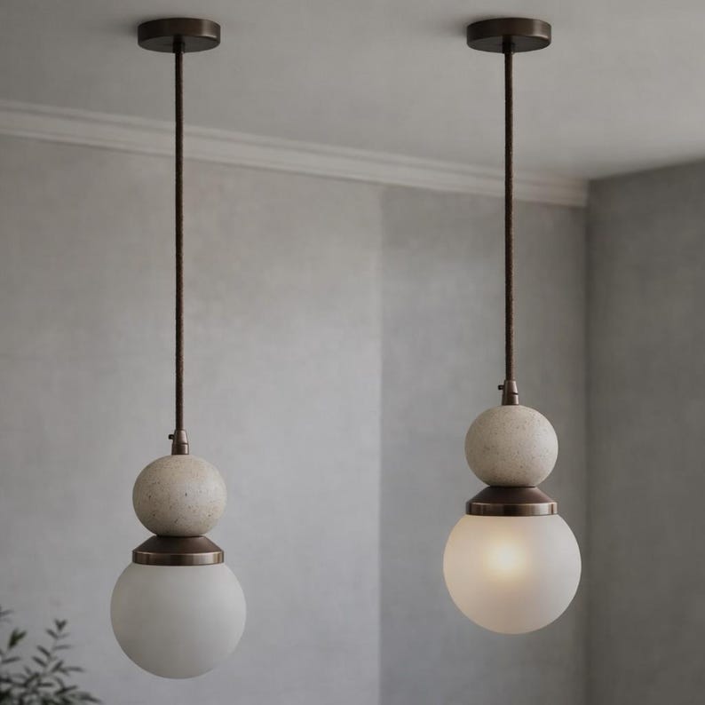 May include: Two pendant lights with a bronze finish. Each light has a frosted glass globe at the bottom, a speckled stone-like sphere above, and a bronze-colored metal accent. The lights hang from a bronze-colored cord.