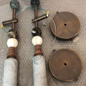 May include: Two decorative lamp fixtures with marble bases, wooden accents, and spherical stone elements. The fixtures have brass-colored metal components and are accompanied by two round, brass-colored ceiling plates.