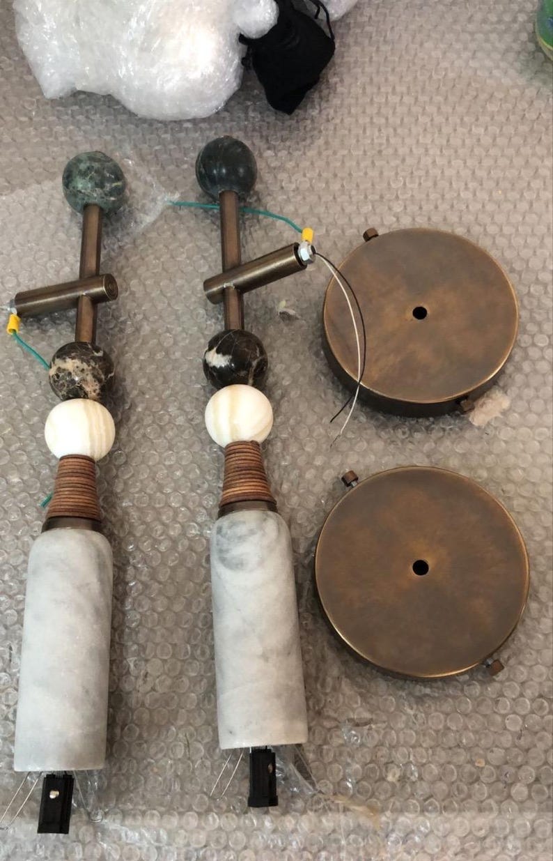 May include: Two decorative lamp fixtures with marble bases, wooden accents, and spherical stone elements. The fixtures have brass-colored metal components and are accompanied by two round, brass-colored ceiling plates.