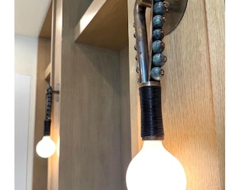 May include: A pair of wall-mounted light fixtures with a unique design. Each fixture features a long, slender arm with a bulb at the end. The arm is adorned with a series of small, blue beads. The fixtures are mounted on a wooden wall.