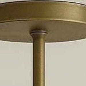 May include: A close-up view of a brass-colored ceiling light fixture. The fixture has a circular base and a central rod extending downwards. The light fixture is mounted on a white ceiling.