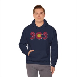 May include: Navy blue hoodie with a front pocket and a drawstring hood. The hoodie features the number "303" in a distressed, vintage style, with the Colorado state flag incorporated into the design. The hoodie is worn by a person.