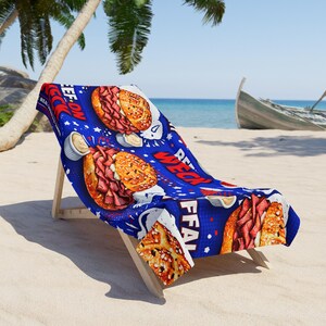 May include: A blue beach towel featuring a repeating pattern of sandwiches, mustard, and text. The text includes the words "REAL" and "FFA". The towel is draped over a wooden beach chair on a sandy beach.