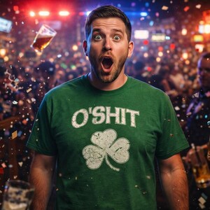 Puede incluir: Un hombre con una camiseta verde con el texto "O'SHIT" y un trébol blanco. Tiene una expresión de sorpresa, con vasos de cerveza y confeti en el aire. La escena sugiere un ambiente festivo.