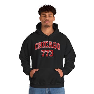 Puede incluir: Sudadera con capucha negra con un bolsillo delantero y el texto "CHICAGO 773" en letras rojas y blancas. La sudadera es de estilo casual.