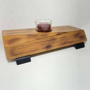 Peut inclure: Un bougeoir en bois avec une finition brun foncé et des pieds en métal noir. Un petit bougeoir en verre pour bougie chauffe-plat se trouve au centre de la base en bois. La bougie est rouge.