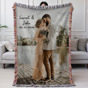 May include: Woven throw blanket featuring a couple embracing, with the names "Sarah & John" and the date "02.22.2010" printed on the front. The blanket has a fringed edge with a multi-colored design. The image depicts a couple on a wooden dock.