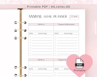 以下が含まれることがあります： ピンクと白の年間目標プランナーで、上部に「ANNUAL GOAL PLANNER」の文字があります。プランナーには、目標、アクションステップ、および「PDF Printable」アイコンのセクションが含まれています。プランナーはA4、Letter、A5サイズ向けに設計されています。