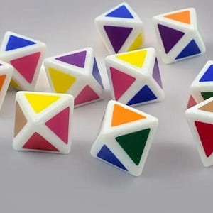 May include: A collection of white, geometric puzzle cubes with colorful triangular faces. Each cube features a unique combination of colors, including blue, purple, orange, yellow, green, and red. The cubes are scattered on a light gray surface.