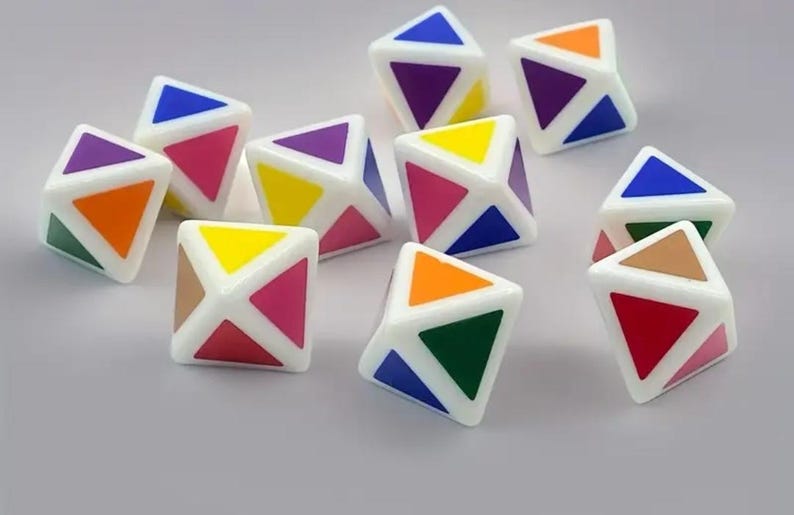 May include: A collection of white, geometric puzzle cubes with colorful triangular faces. Each cube features a unique combination of colors, including blue, purple, orange, yellow, green, and red. The cubes are scattered on a light gray surface.