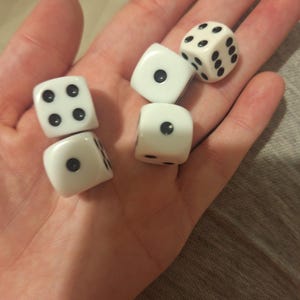May include: Five white dice with black dots are displayed in an open palm. The dice are in various positions, showing different numbers of dots. The dice are a classic gaming accessory.
