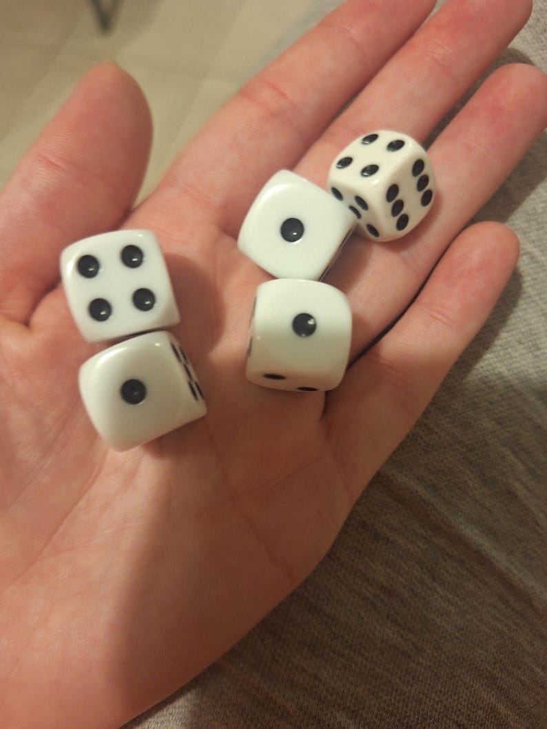 May include: Five white dice with black dots are displayed in an open palm. The dice are in various positions, showing different numbers of dots. The dice are a classic gaming accessory.