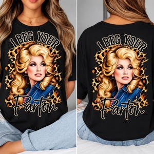 Könnte beinhalten: Ein schwarzes T-Shirt mit einem Grafikdruck einer blonden Frau mit voluminösem Haar, die ein Jeanshemd trägt. Hinter dem Porträt befindet sich ein Leopardenmuster. Der Text "I BEG YOUR Parton" ist in weißer und schwarzer Schrift gedruckt.